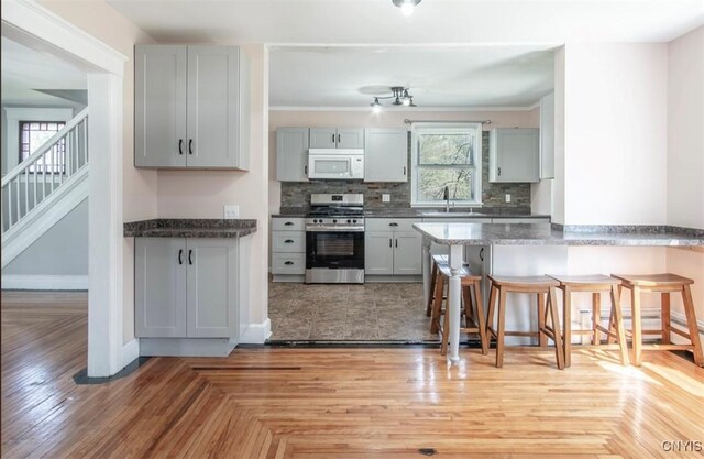 83 Salisbury St, Sandy Creek, NY 13083 - kitchen with a sink, white microwave, a kitchen bar, gas range, and gray cabinetry