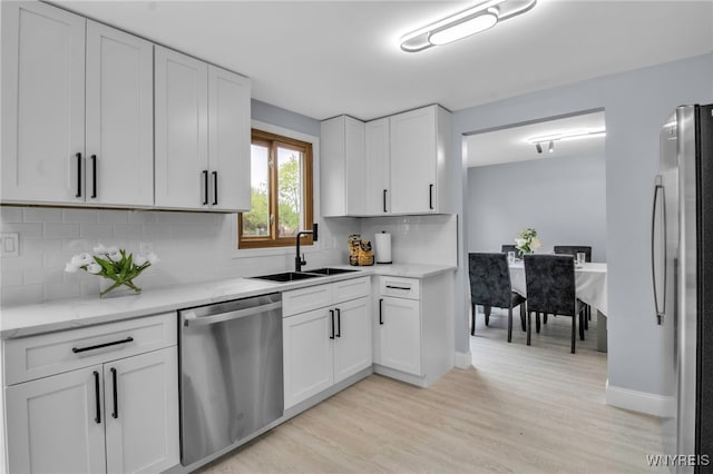kitchen featuring light wood finished floors, a sink, white cabinets, stainless steel appliances, and tasteful backsplash