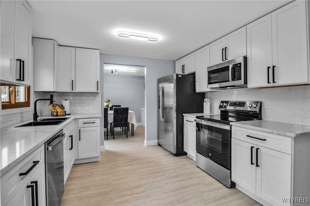 kitchen with light wood finished floors, a sink, stainless steel appliances, light stone countertops, and decorative backsplash