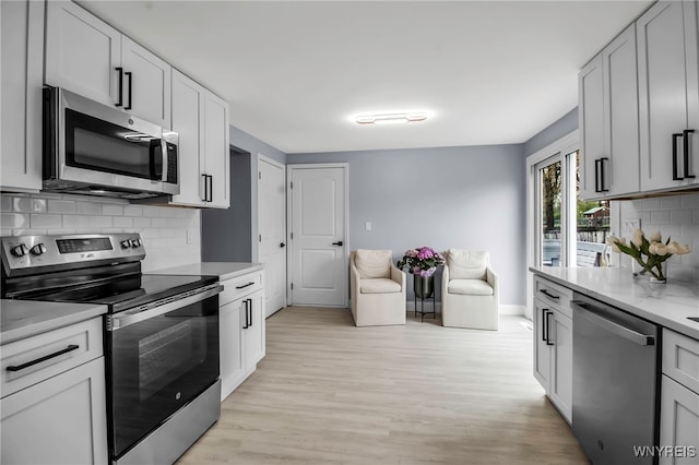 kitchen featuring baseboards, light wood finished floors, decorative backsplash, light countertops, and appliances with stainless steel finishes