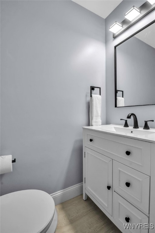 bathroom featuring toilet, baseboards, vanity, and wood finished floors