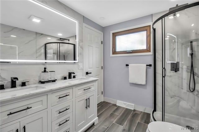 bathroom featuring a sink, double vanity, a marble finish shower, and baseboards