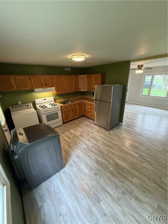 kitchen with freestanding refrigerator, under cabinet range hood, white gas stove, separate washer and dryer, and light wood-type flooring