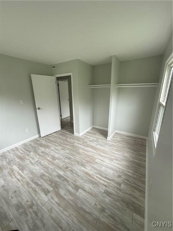 unfurnished bedroom featuring baseboards, a closet, visible vents, and wood finished floors