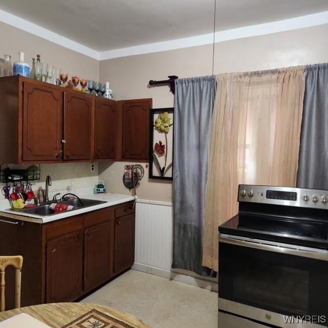kitchen with light floors, a sink, a wainscoted wall, stainless steel range with electric stovetop, and light countertops
