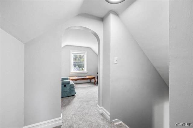 hallway featuring baseboards, carpet flooring, and vaulted ceiling