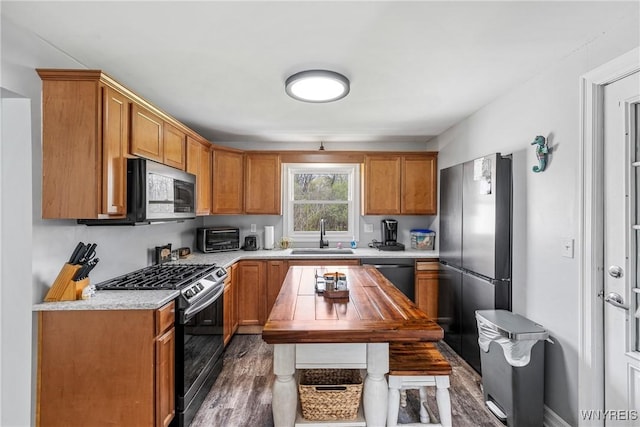 kitchen featuring wood finished floors, brown cabinets, a sink, light countertops, and appliances with stainless steel finishes