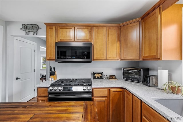 kitchen with a sink, brown cabinetry, stainless steel appliances, light stone counters, and a toaster
