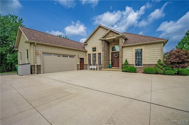 view of front facade with stone siding, a shingled roof, an attached garage, and driveway