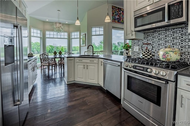 kitchen featuring dark wood-style flooring, a sink, a peninsula, dark countertops, and stainless steel appliances