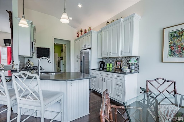 kitchen with lofted ceiling, tasteful backsplash, a breakfast bar, high quality fridge, and dark countertops