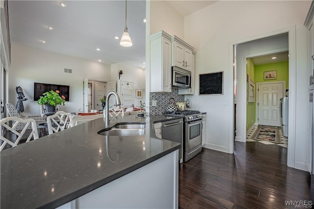 kitchen featuring dark stone countertops, a sink, stainless steel appliances, backsplash, and dark wood-style floors