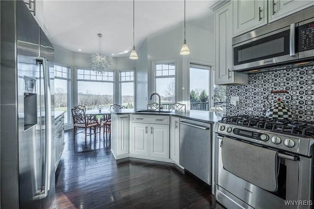 kitchen with a sink, a peninsula, dark wood-type flooring, stainless steel appliances, and tasteful backsplash