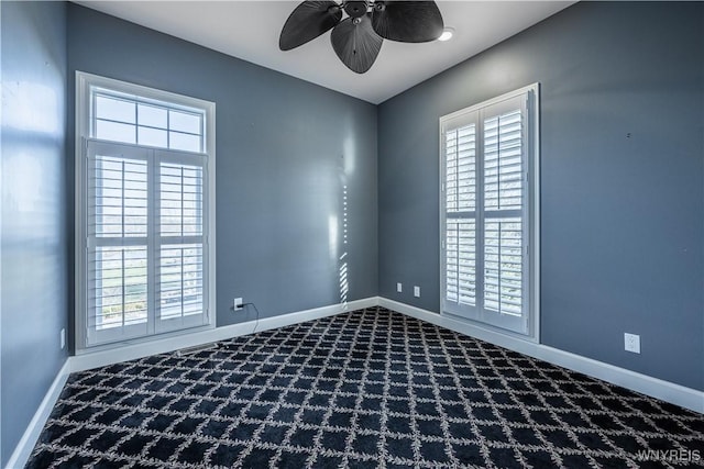 empty room with ceiling fan, a wealth of natural light, and dark carpet
