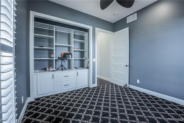 interior space with a ceiling fan, baseboards, dark colored carpet, and visible vents