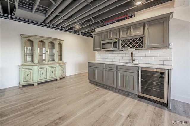 bar with wine cooler, light wood-style flooring, stainless steel microwave, a sink, and wet bar