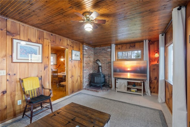 living room with a ceiling fan, a wood stove, wooden walls, and wood ceiling