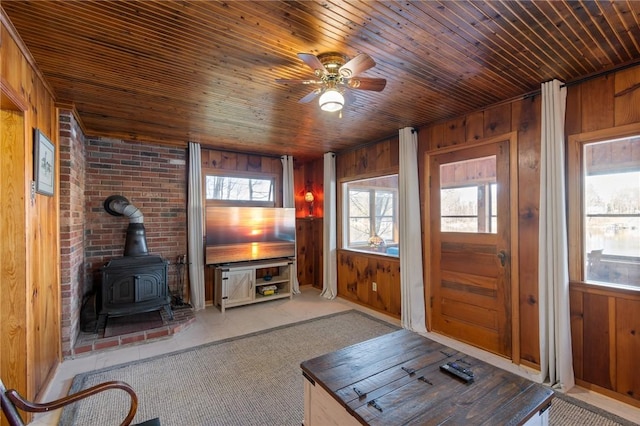 carpeted living room with a wood stove, a wealth of natural light, wooden ceiling, and wood walls