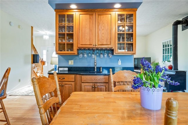 kitchen with glass insert cabinets, a sink, wood finished floors, brown cabinets, and a wood stove