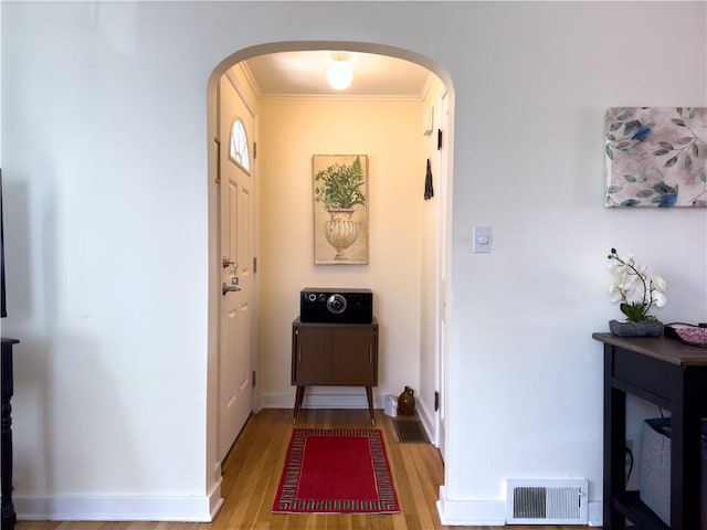 doorway to outside featuring ornamental molding, light wood-type flooring, visible vents, and arched walkways