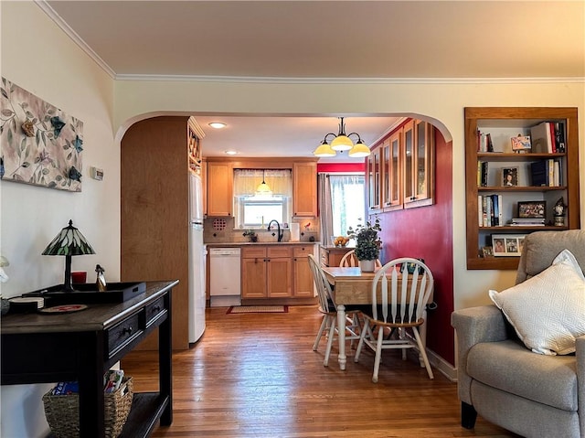 dining area with arched walkways, crown molding, and wood finished floors