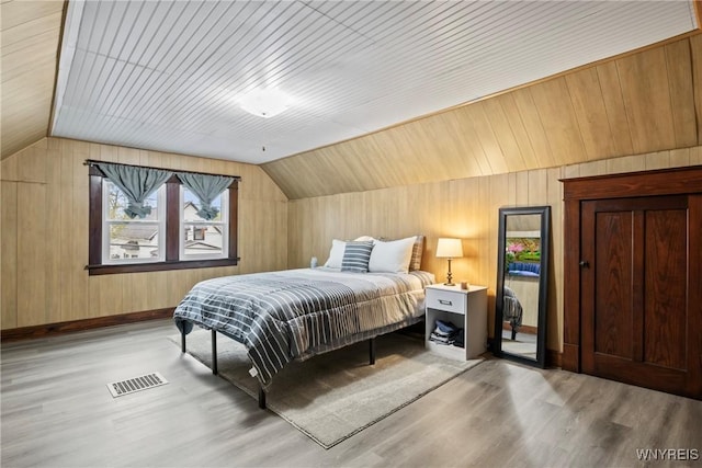 bedroom featuring vaulted ceiling, wood walls, visible vents, and wood finished floors