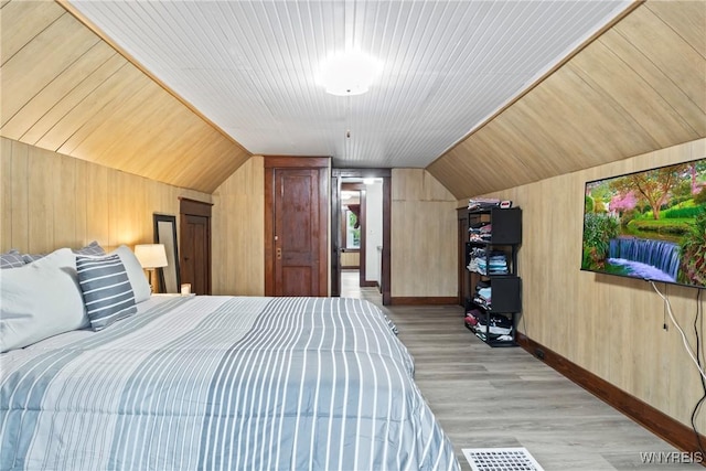 bedroom featuring baseboards, wooden walls, light wood finished floors, and vaulted ceiling