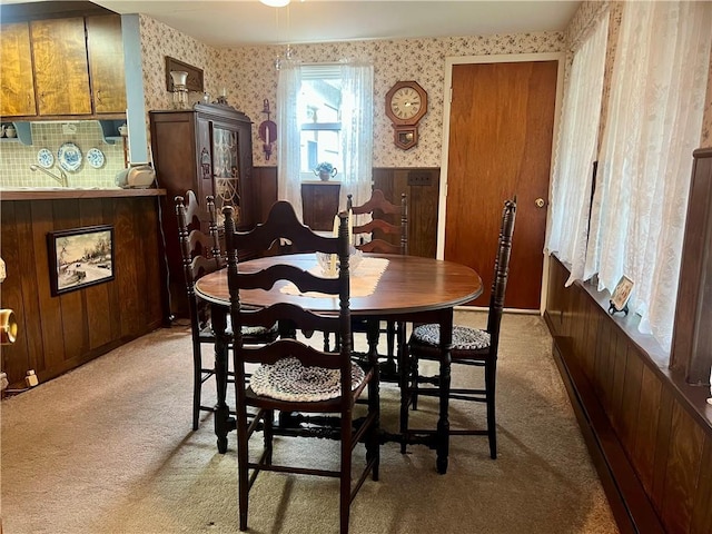 dining space featuring light colored carpet, wooden walls, and wallpapered walls