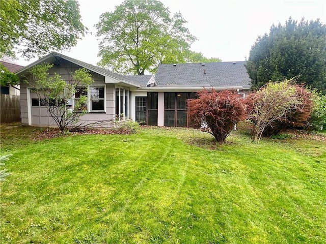 rear view of house featuring a yard, roof with shingles, and a sunroom