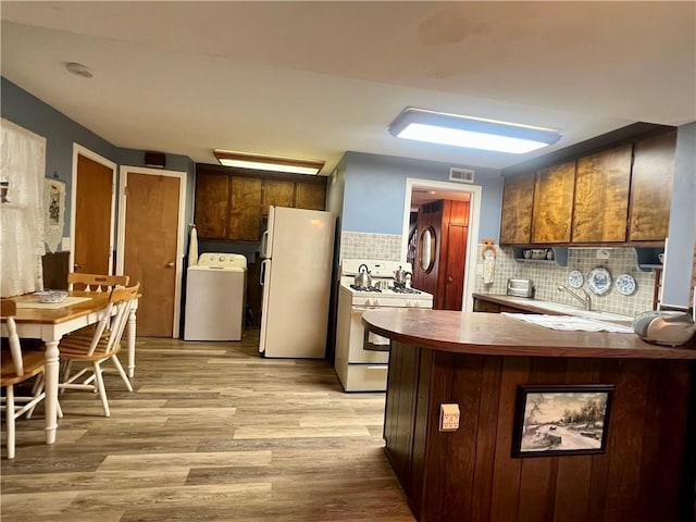 kitchen with washer / clothes dryer, white appliances, visible vents, backsplash, and light wood-style floors