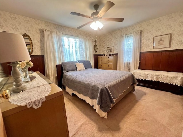 carpeted bedroom with wallpapered walls, a wainscoted wall, and ceiling fan