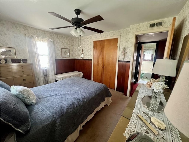 carpeted bedroom with a wainscoted wall, visible vents, and wallpapered walls