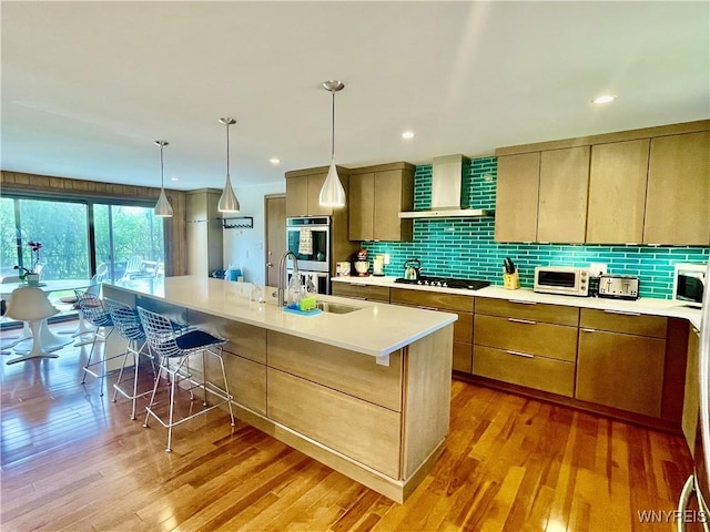 kitchen with wall chimney range hood, double oven, light wood-type flooring, and a sink