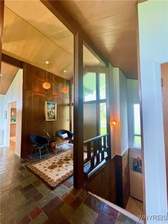 corridor featuring wood ceiling, plenty of natural light, lofted ceiling with beams, and stone tile flooring