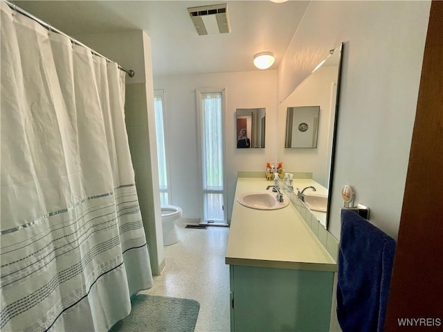 bathroom featuring a sink, toilet, visible vents, speckled floor, and double vanity