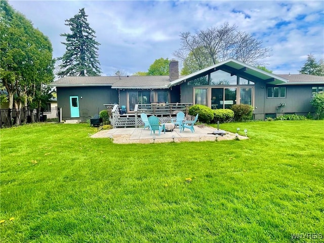 back of property featuring a chimney, a lawn, fence, a patio, and a wooden deck