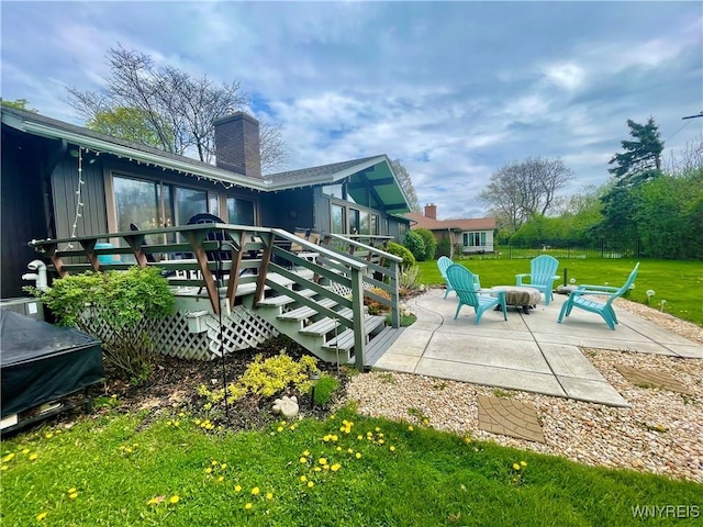 rear view of property with a chimney, a wooden deck, a lawn, fence, and a patio area