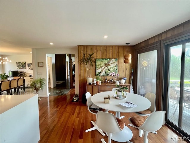 dining room featuring a chandelier, recessed lighting, wooden walls, and wood finished floors