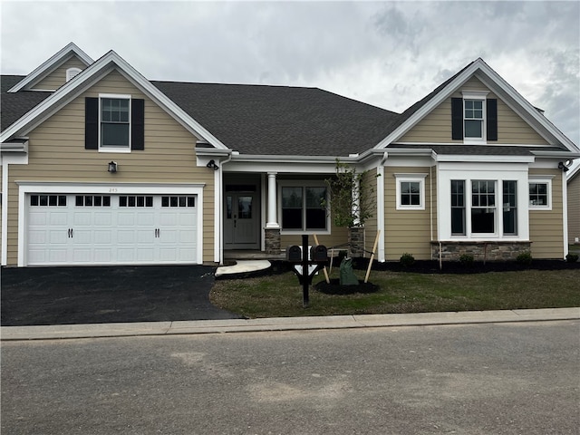 view of front of property with roof with shingles, a front yard, stone siding, and driveway