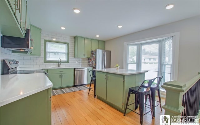 kitchen with stainless steel appliances, a breakfast bar, a sink, green cabinetry, and light countertops
