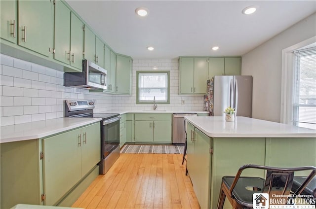 kitchen with stainless steel appliances, green cabinets, a sink, decorative backsplash, and light countertops
