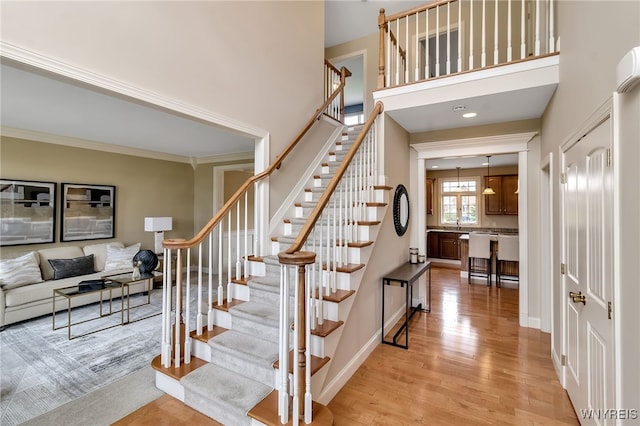 stairway with ornamental molding, wood finished floors, and a high ceiling