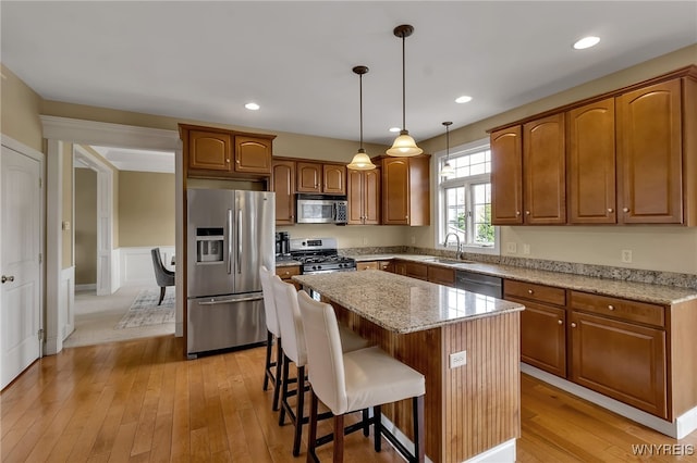 kitchen featuring a sink, appliances with stainless steel finishes, a center island, light stone countertops, and light wood-style floors