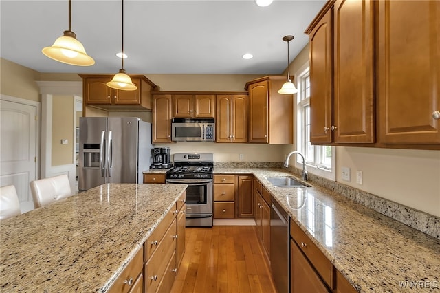 kitchen featuring appliances with stainless steel finishes, brown cabinetry, light stone counters, a sink, and light wood-type flooring