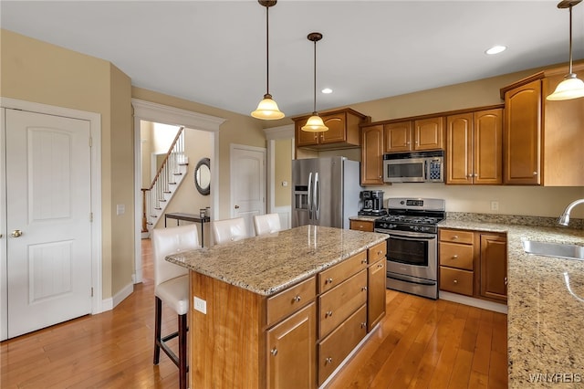 kitchen featuring stainless steel appliances, light wood-style flooring, a sink, and light stone countertops