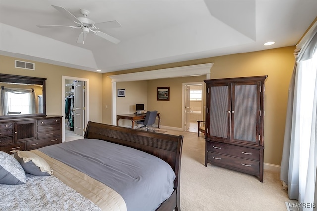 bedroom with light colored carpet, multiple windows, a walk in closet, and a tray ceiling