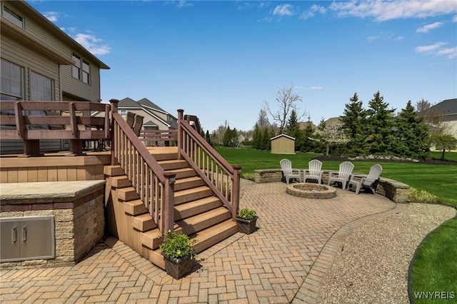 view of patio featuring an outdoor structure, stairway, a wooden deck, a fire pit, and a storage shed