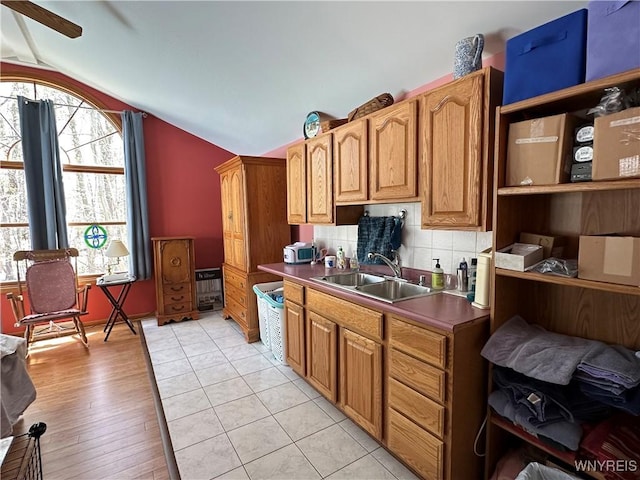 kitchen featuring a sink, lofted ceiling, ceiling fan, light wood-style flooring, and decorative backsplash
