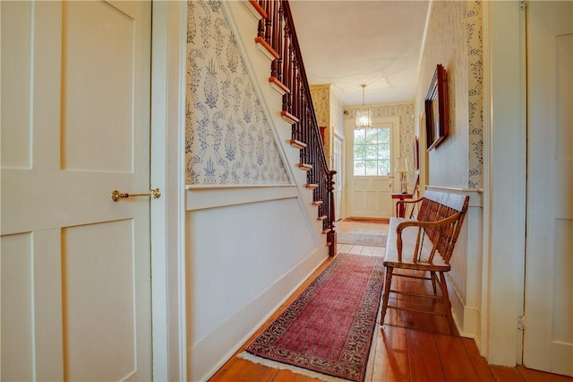 corridor with stairway, a decorative wall, wallpapered walls, and wood finished floors