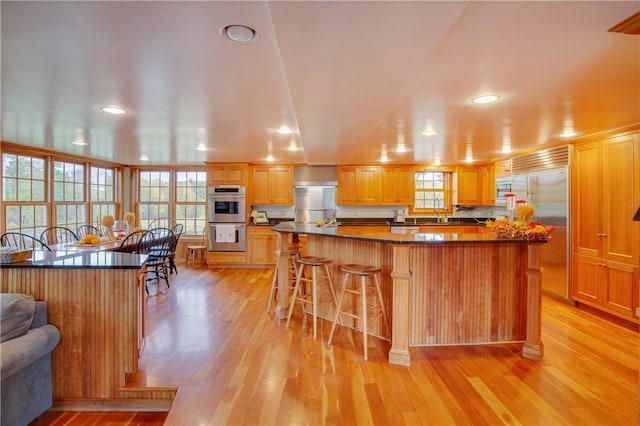 kitchen featuring appliances with stainless steel finishes, plenty of natural light, a kitchen breakfast bar, and light wood-style floors
